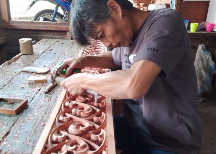 Beni saat mengerjakan ukiran bermotif lapiak ameh batang padi di Workshop Ukir Kayu Chan Umar. (SumbarKita/Rian)